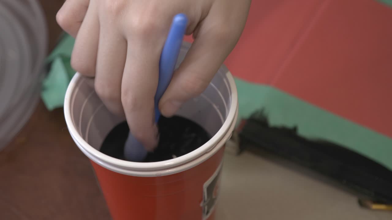 Hand Of A Painter Dipping The Used Paintbrush On The Water On Red Cup.-closeup shot