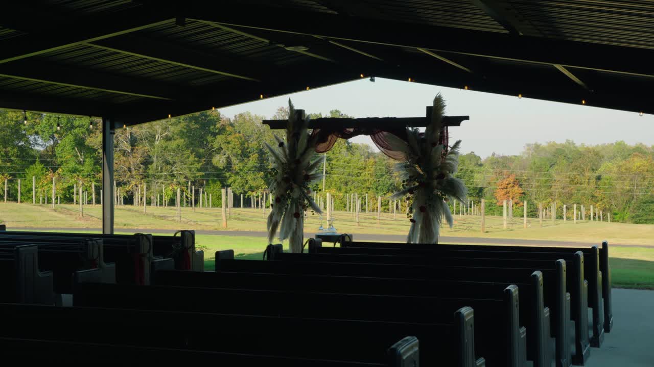 A cinematic gimbal shot moving toward a beautifully decorated ceremony arch with a vineyard in the background, capturing the serene wedding setting.