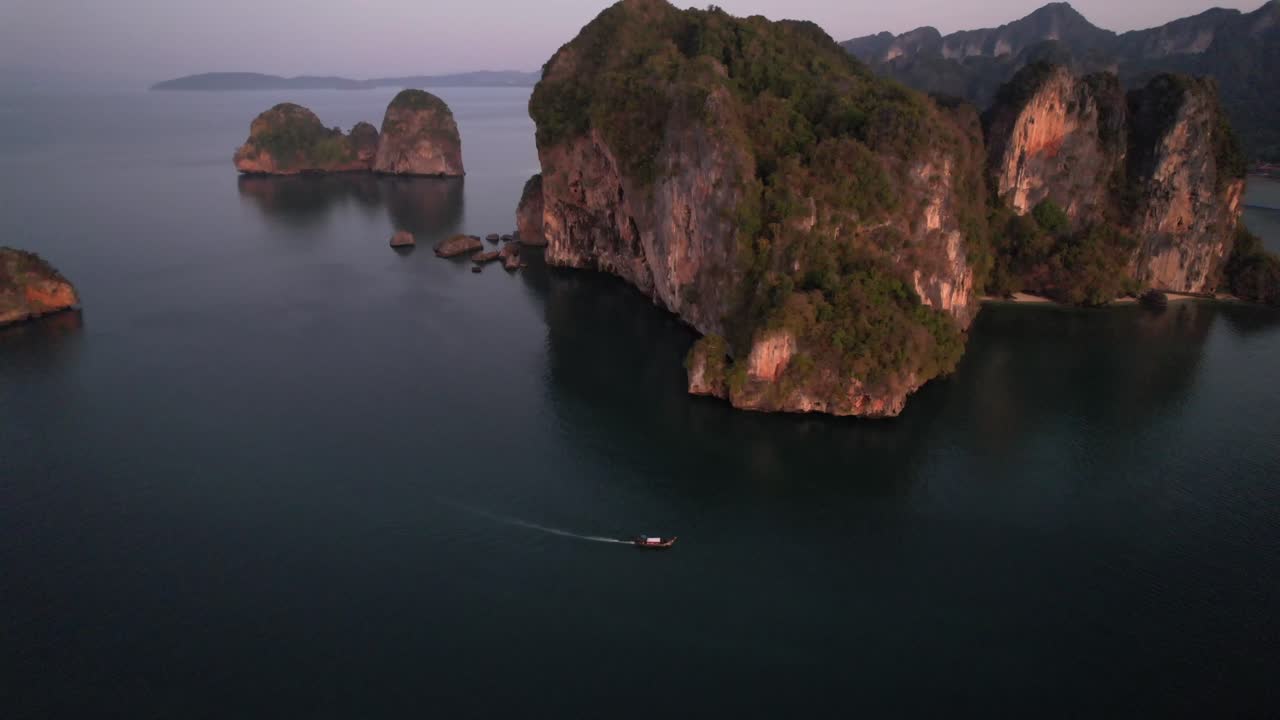 amplio drone aéreo de gran altitud de formaciones montañosas de piedra caliza únicas cerca de la playa railay en krabi tailandia durante el amanecer como un barco tailandés de cola larga en el mar de andamán
