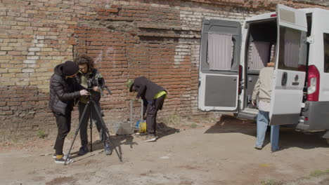 two production co workers setting up a camera in the street and other two workers taking material for a recording from a van