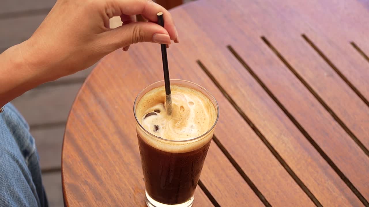 Closeup of Woman with Perfectly Manicured Nails, Touching Straw of Iced Coffee on Sunny Cafe Veranda
