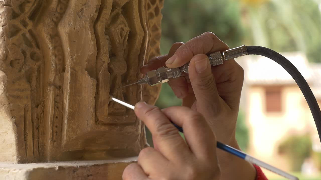 Primer plano detallado de un restaurador experto limpiando a fondo un elemento decorativo de piedra con una herramienta neumática de precisión
