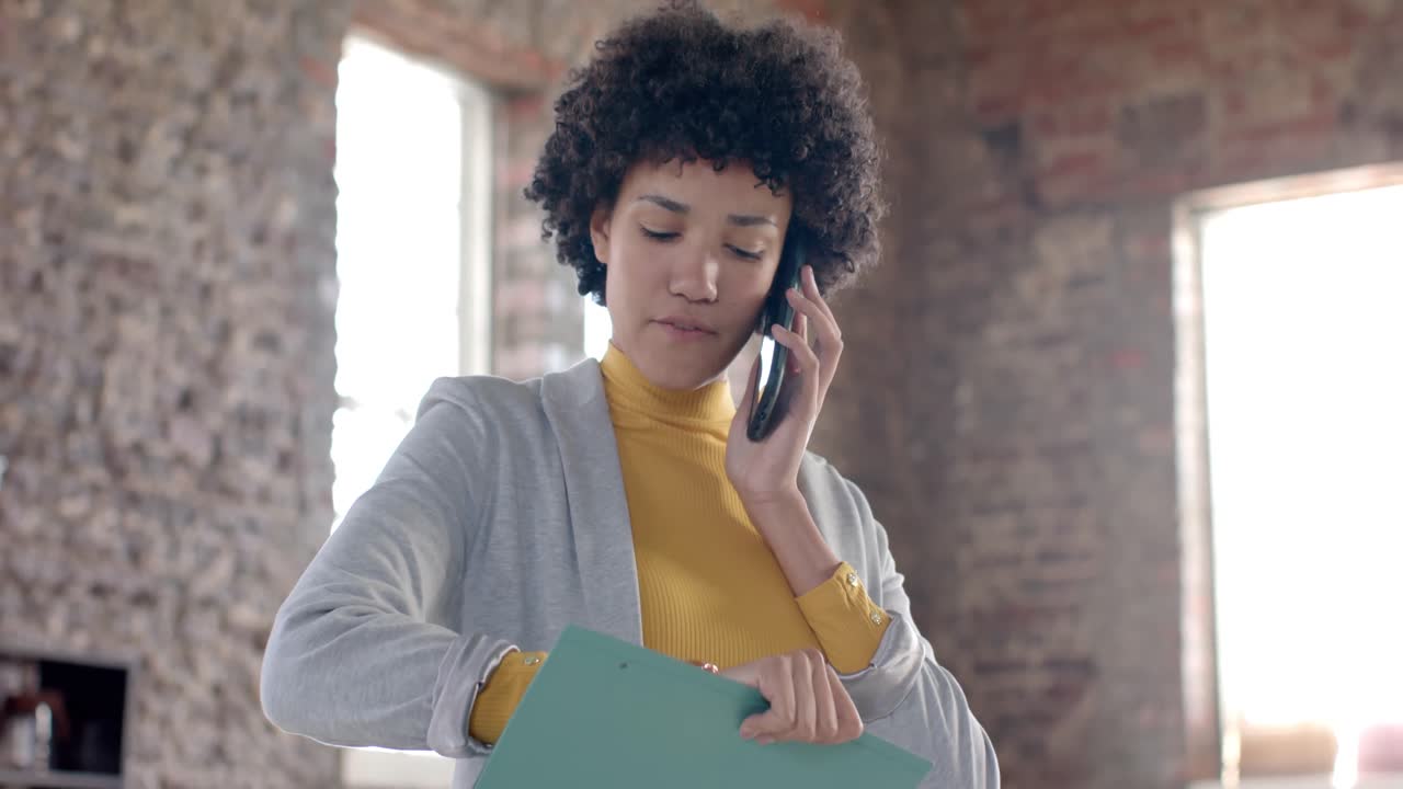 Fokuseret afslappet forretningskvinde af blandet herkomst taler i smartphone og holder fil i slow motion