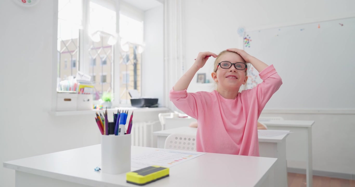 Bambina felice con gli occhiali alza la mano in classe