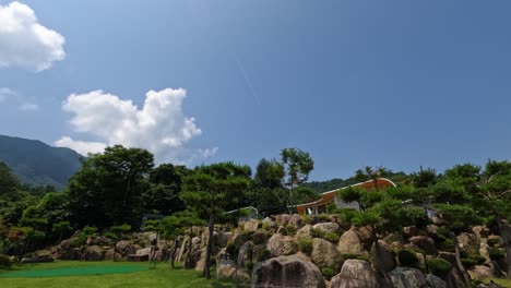 a beautiful time-lapse on a clear sunny day at a luxury glamping resort in gapyeong, showing clouds moving across a blue sky above a landscaped rock garden and mountain