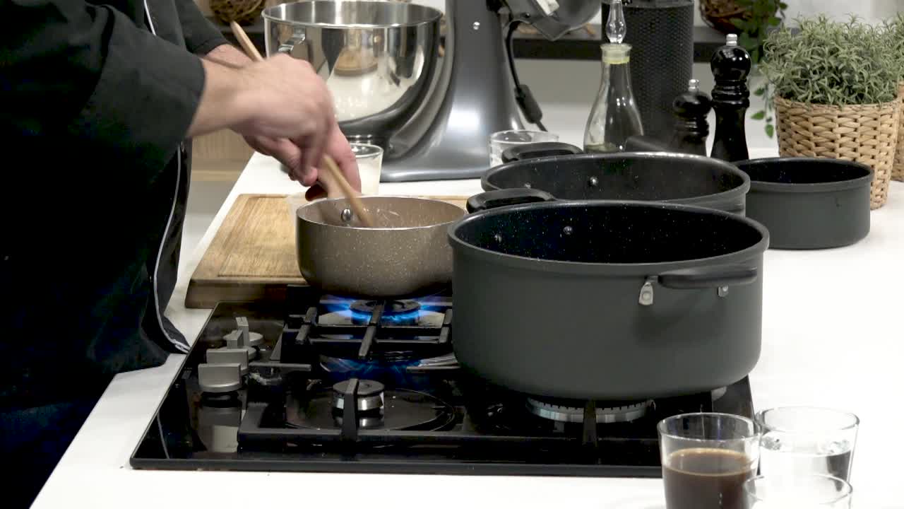 Demonstration of culinary techniques in a sleek kitchen. A chef skillfully stirs ingredients in a saucepan while preparing various dishes. The setup includes multiple cooking pots