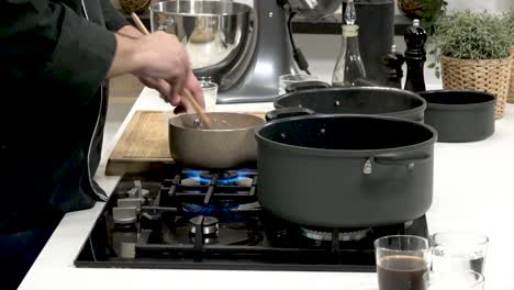 demonstration of culinary techniques in a sleek kitchen. a chef skillfully stirs ingredients in a saucepan while preparing various dishes. the setup includes multiple cooking pots