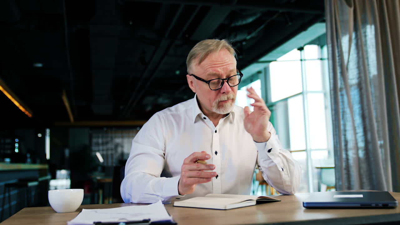 Puzzled senior man thinking over the problem. Businessman taking some notes into the paper book. Low angle view.