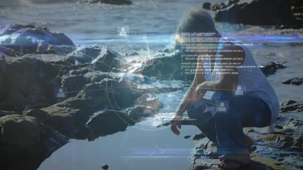 Sitting on rocks by ocean, elderly person viewing animation of digital network