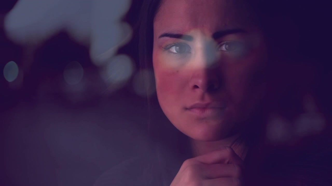 Donna adulta che apre gli occhi mentre una banda luminosa scorre sul vetro, una mano che si alza e scintilla, mettendo a fuoco per un film.