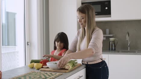 niña ayudando a su madre a cocinar ensalada para la cena