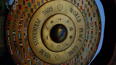 vertical slow-motion parallax shot of the world peace gong in bali, a symbol of global unity and harmony, showcasing various national flags and religious signs