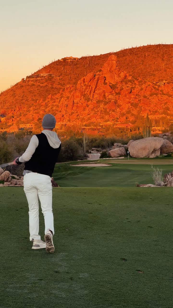 Golfer hits low stinger iron shot at sunrise and shrugs on beautiful desert golf course with red mountain backdrop, 4k vertical winter golf