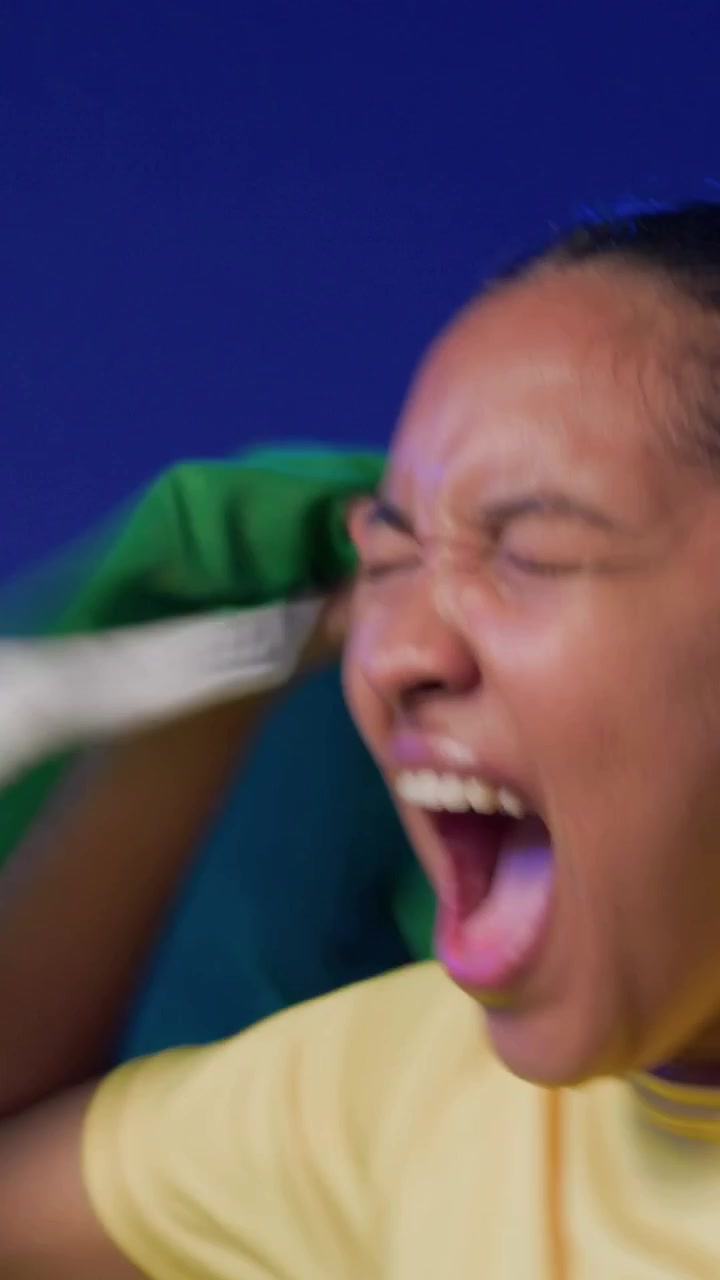 Vertical video: Waving woman in yellow shirt pulling flag up and cheering at set, showing support