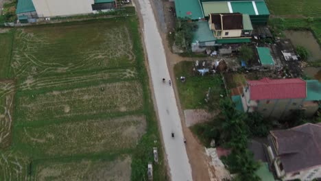 countryside drone birds eye view of motorbike driving in straight long highway between houses and rice field in rural, vietnam