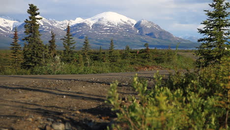 snow covered mountains in background of dirt road in alaska wilderness