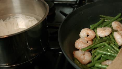 noodles boiling next to king prawns with green beans in hot pan