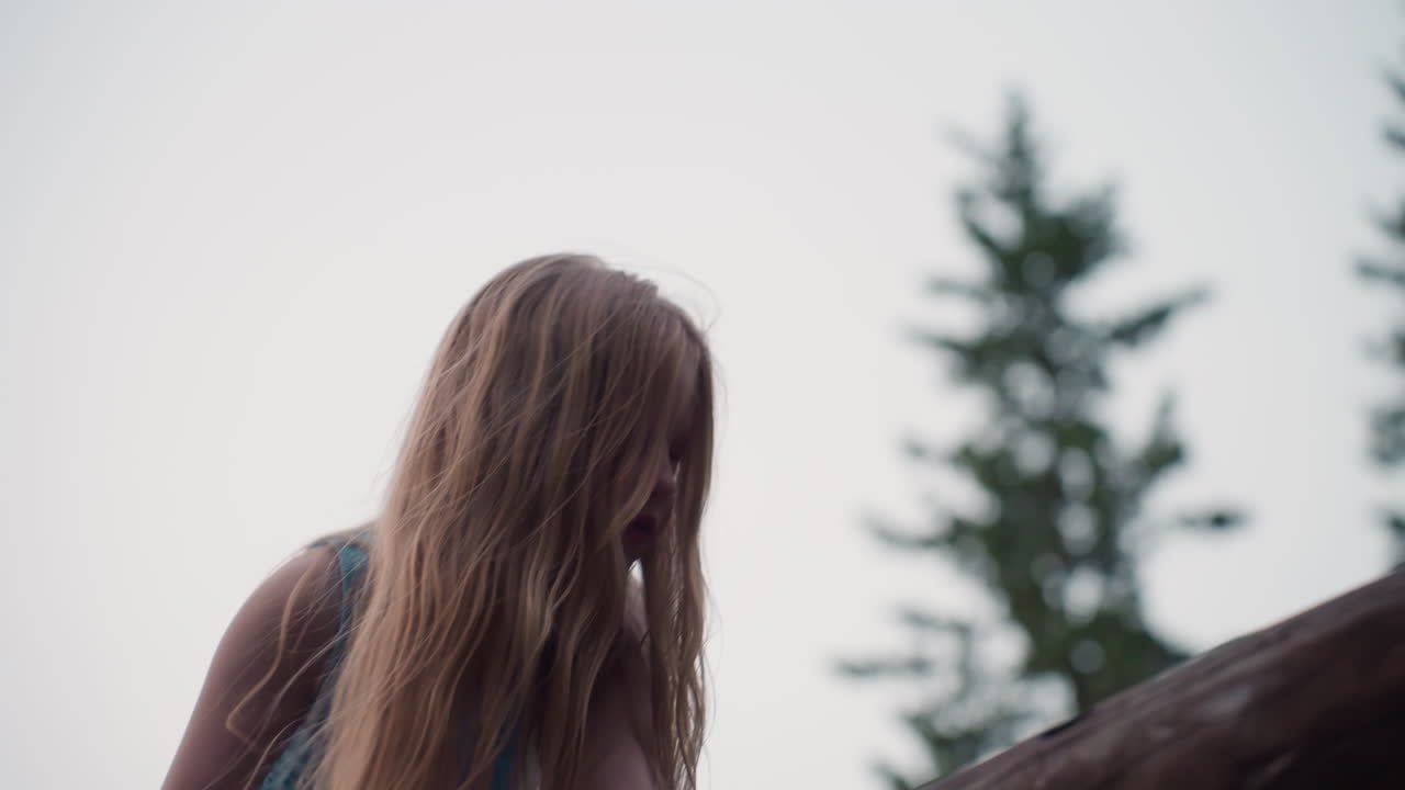 side view of teenage girl in blue dress climbing fallen log on playground structure at dusk showcasing adventurous spirit and balance skills amid lush green park setting in summer evening