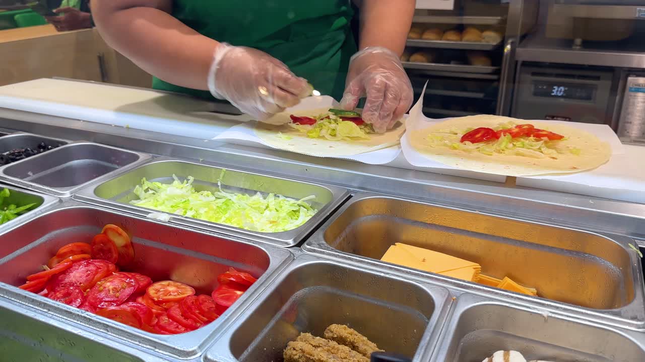 Un lavoratore con guanti di plastica prepara wrap di tortilla freschi con lattuga e pomodori a Bangkok.
