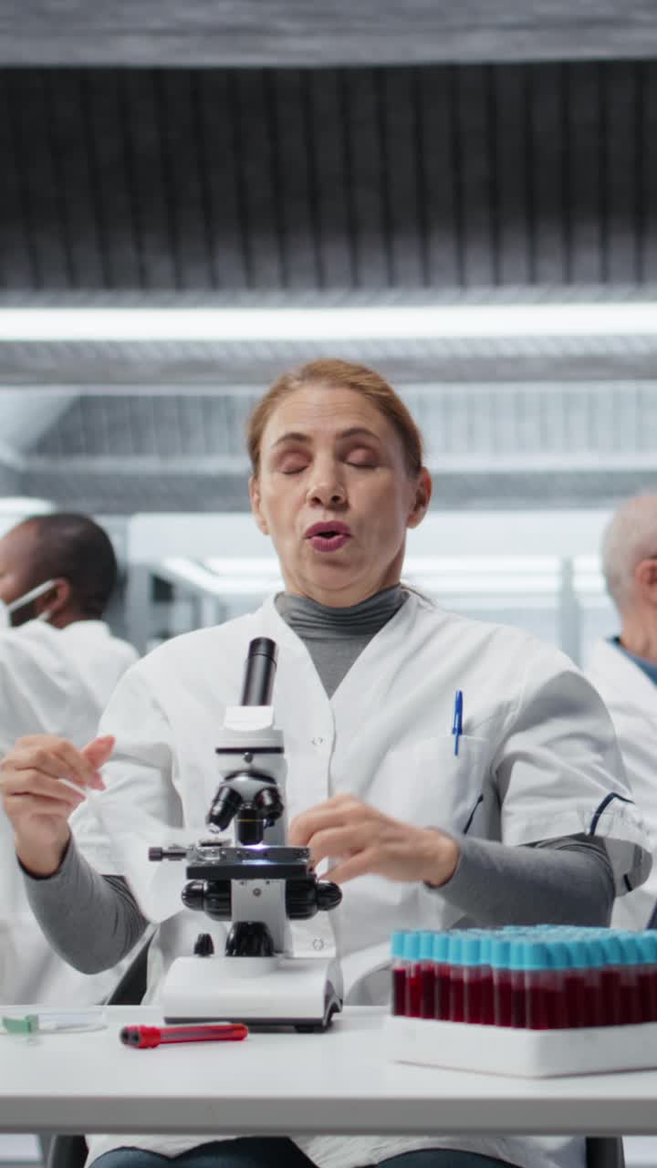 Técnico de vídeos verticais usando máscara cirúrgica e examinando lâminas de patologia sob microscópio
