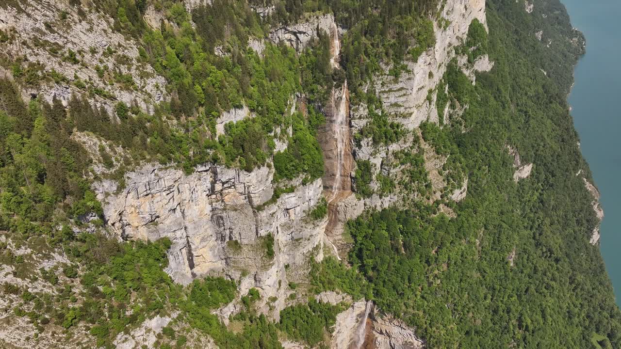 A striking view of Seerenbachfälle, Switzerland, showcases multiple waterfalls cascading down vast, green-clad cliffs, with glimpses of a turquoise lake