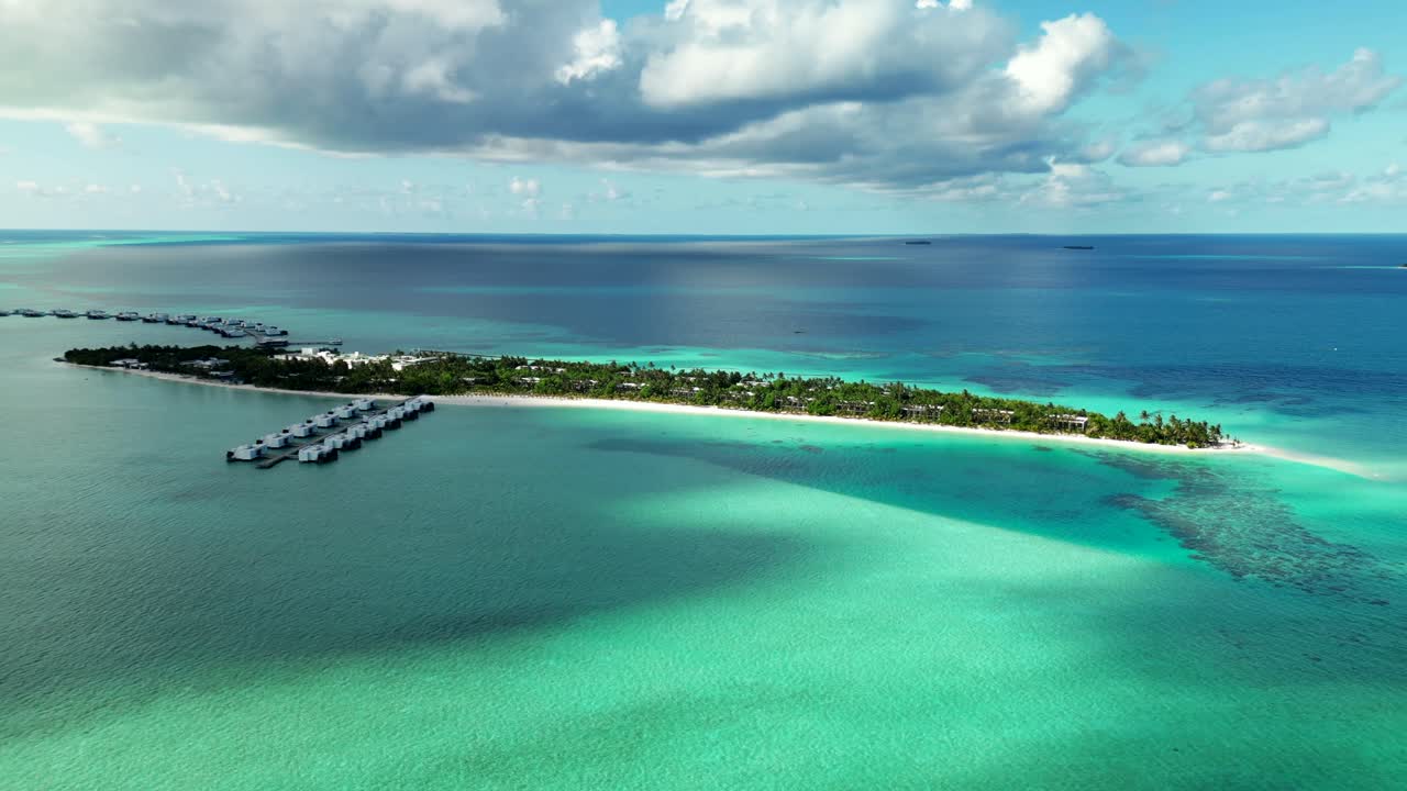 Isola delle Maldive con bungalow sull'acqua, spiaggia bianca e laguna turchese sotto un cielo nuvoloso