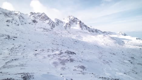 Vista-Aérea-Del-Paisaje-Montañoso-Cubierto-De-Nieve-En-Un-Día-Soleado-Con-Nubes-Rodando-Detrás-En-Fluela-Pass,-Suiza