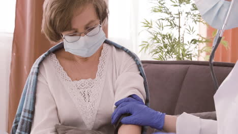 female doctor takes the pulse of an elderly patient sitting on a sofa