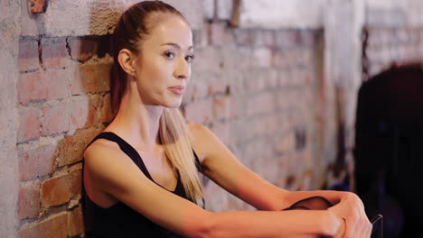 Sporty-Young-Woman-Using-Mobile-Phone-While-Resting-During-Break-At-Gym