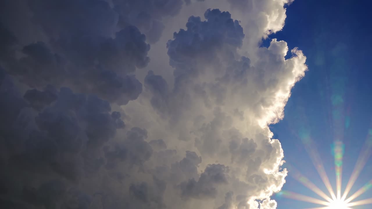 Dramatic low-angle shot of towering clouds against a bright sunburst in a clear blue sky, perfect