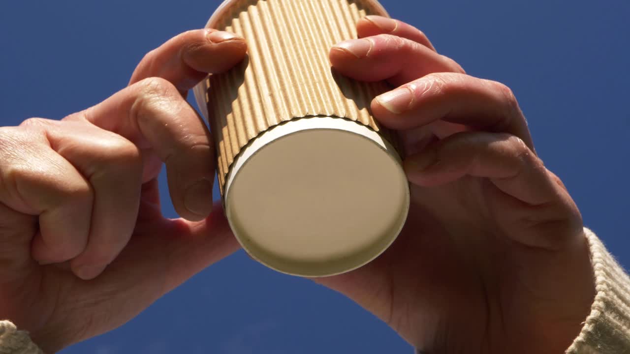 Two hands holding takeout coffee against blue sky close up shot