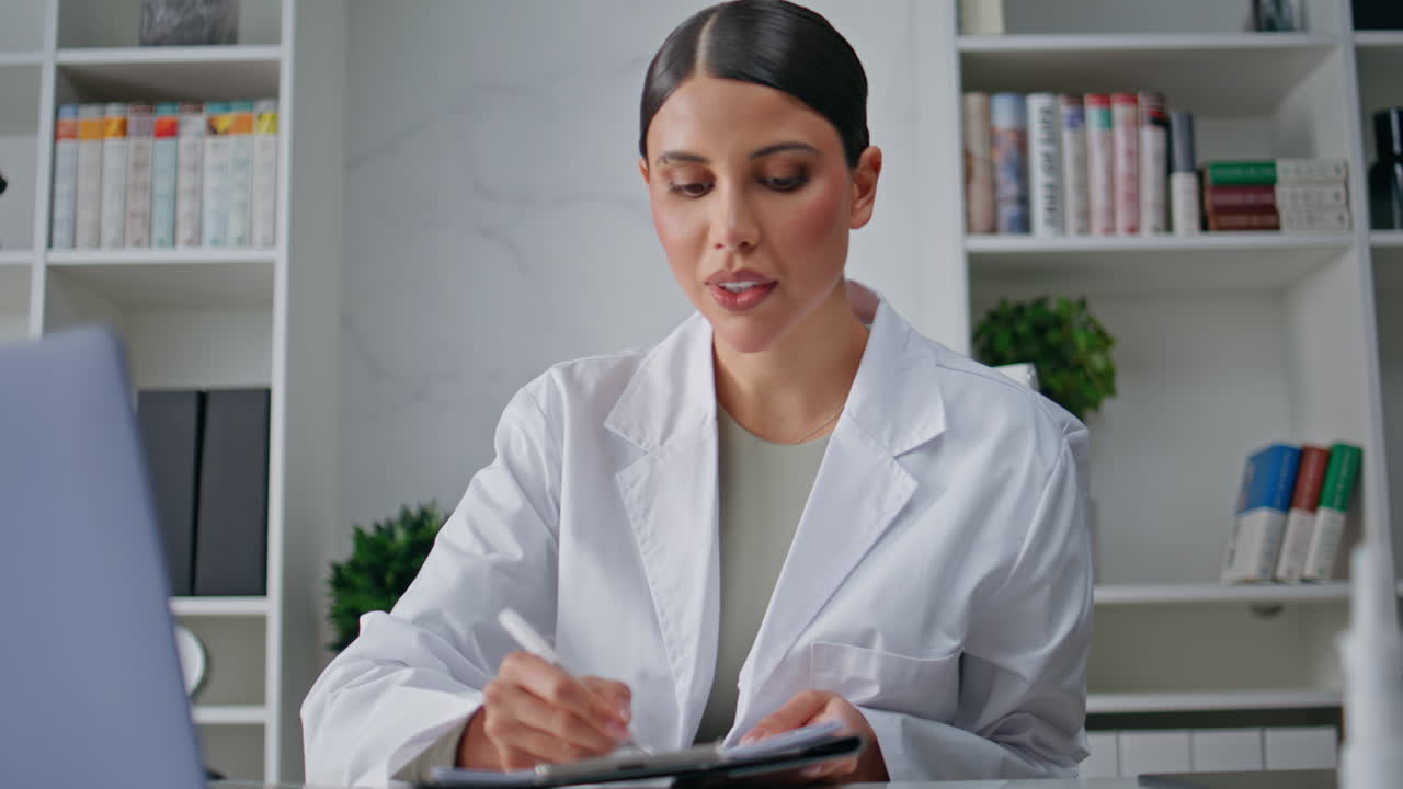 Doctor providing video meeting by laptop in clinic closeup. Woman consulting