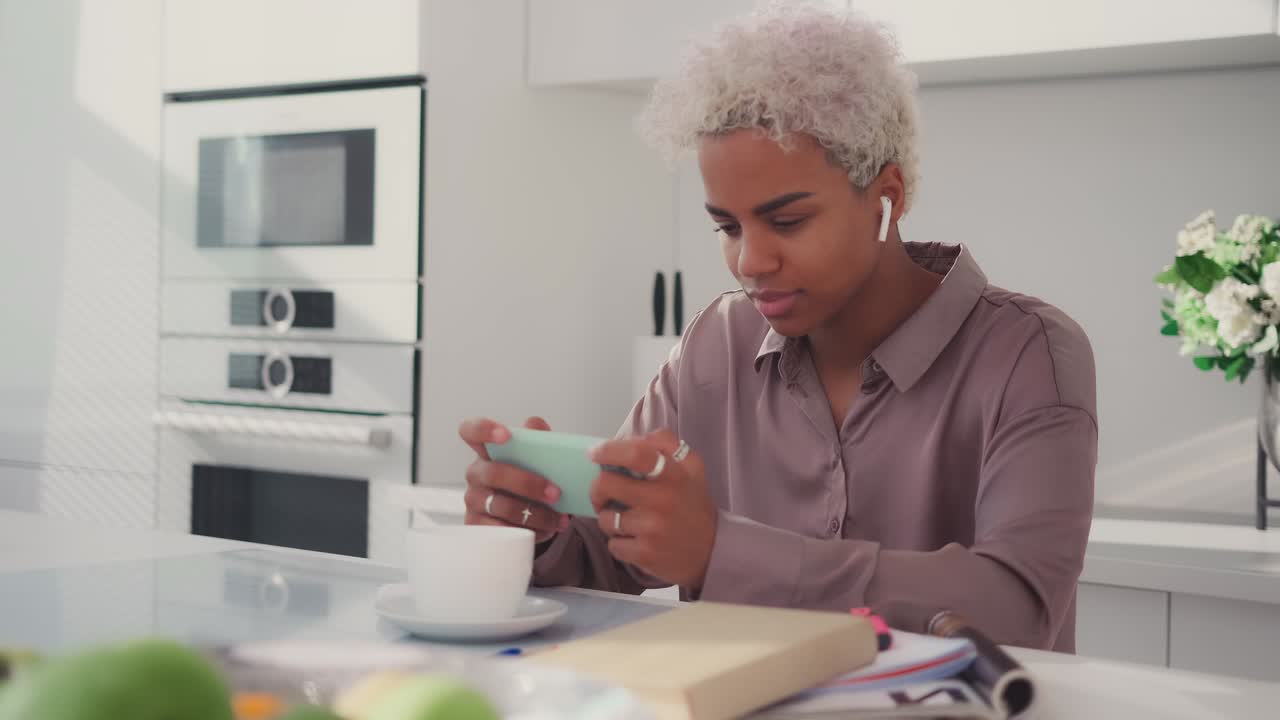 Smiling young african woman using phone spend free leisure time in kitchen