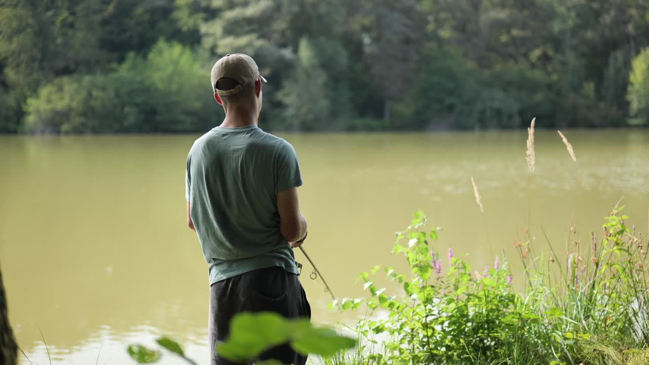 Young angler stands at the edge of murky lake surrounded by trees
