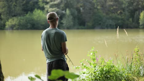 Young-angler-stands-at-the-edge-of-murky-lake-surrounded-by-trees