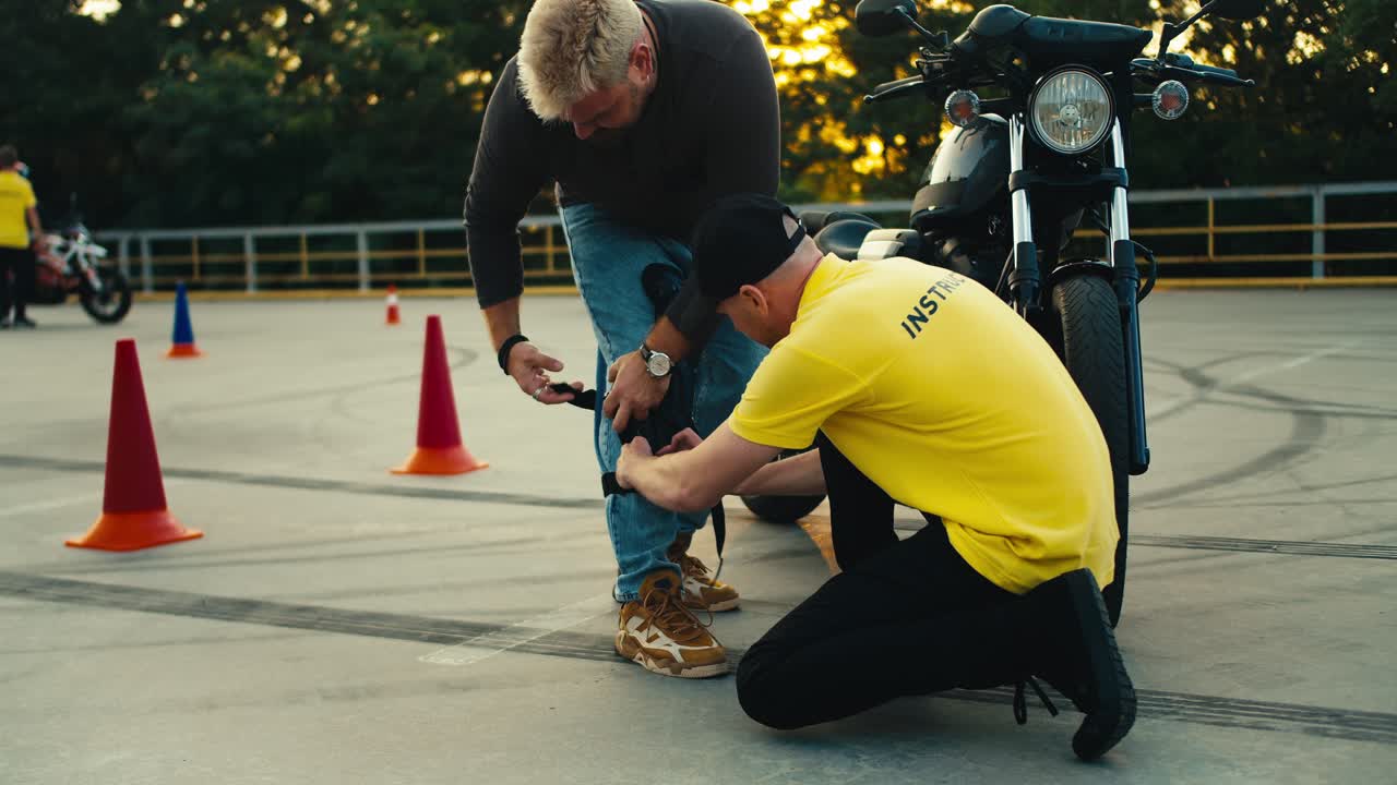 instructor de conducción en camiseta amarilla ayuda a un joven motociclista a ponerse rodilleras. motocicleta e instructor de conducción de bicicletas