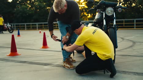 driving instructor in yellow t-shirt helps young biker put on knee pads. motorcycle and bike driving instructor