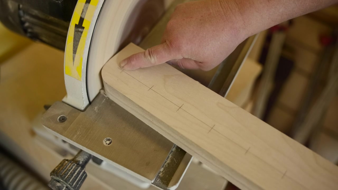 Mani che levigano un corrimano in legno curvo in officina, levigatrice a disco di precisione che liscia una striscia di acero marcata, tracciato a matita. Media