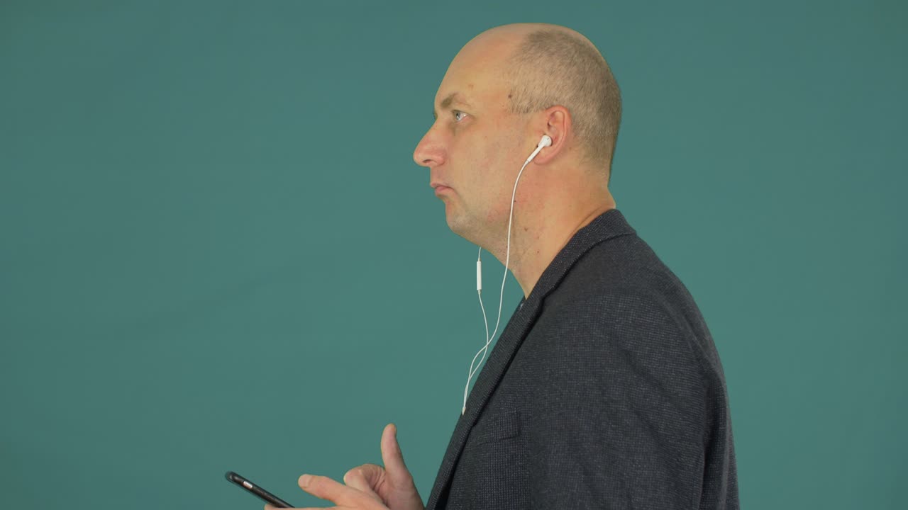 Bald man using mobile phone for listening music in headphones profile view