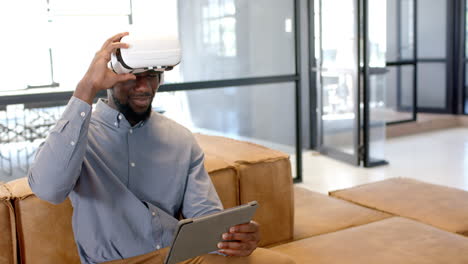 using vr headset, man holding tablet while sitting on couch in office