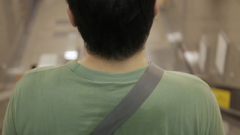 view of back of asian man while using escalator getting to subway station