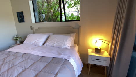 dolly push view of queen size bed below open window, lamp and glass sliding doors in minimalist airbnb, queenstown, otago new zealand