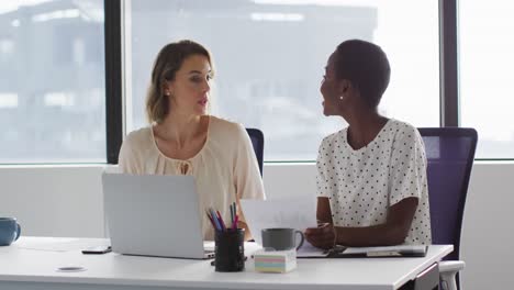 two diverse female colleagues looking at laptop and discussing in office