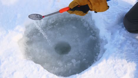 la mano del pescador limpia el agujero de la cuchara del hielo para la pesca de invierno