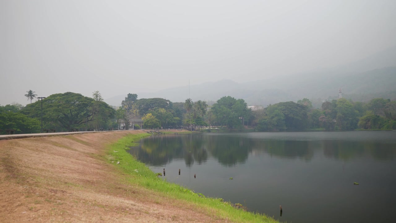 Ampia veduta paesaggistica del riflesso del bacino idrico di Ang Kaew presso l'Università di Chiang Mai, con il monte Doi Suthep nascosto dietro una densa foschia di inquinamento atmosferico durante la stagione del fumo in Thailandia