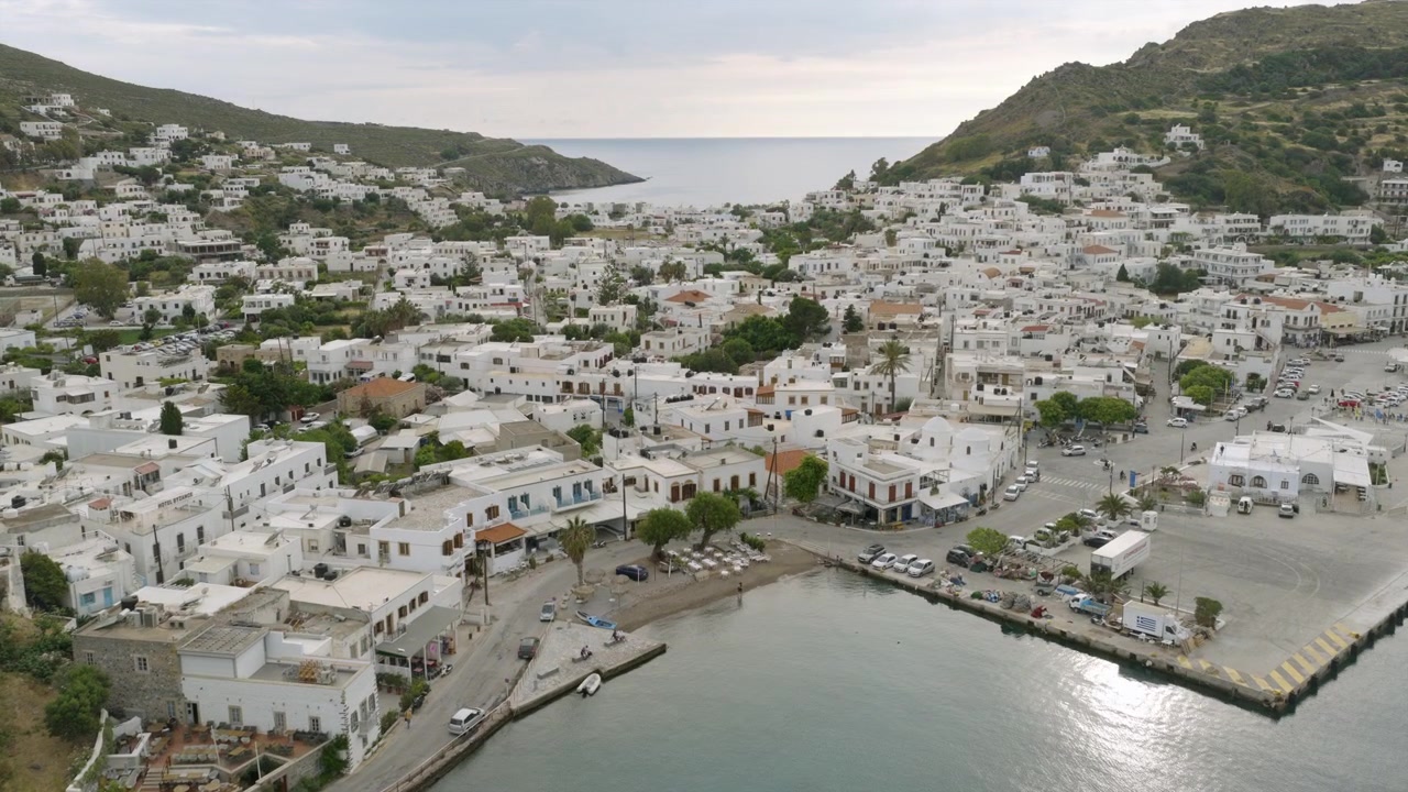 Patmos'un Skala kıyı şeridinin havadan yakın çekimi, badanalı binaları, küçük bir limanı ve sakin Ege sularını gösteriyor.