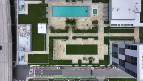 ascending top down shot of high-rise residential complex with private swimming pool near highway of miami city,usa.traffic on intersection during daytime. modern skyscraper in modern urban development
