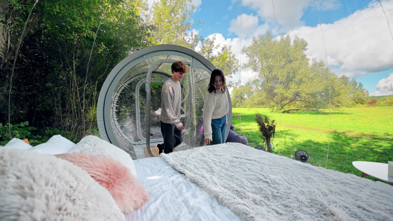 Una coppia che parla ed entra in una tenda a bolla trasparente in un sito di glamping, vista dall'interno. Rigogliosa foresta circostante