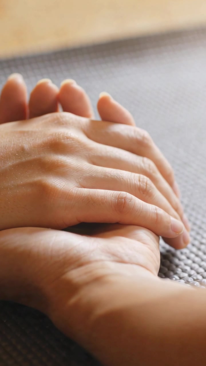 Vertical video: Placing adult hand palm-down over child hand on textured mat, showing calm comfort