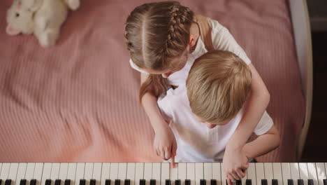 blonde girl holds brother fingers and plays melody on piano